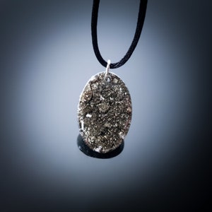 May include: A silver oval pendant necklace with a black cord. The pendant is filled with a sparkly, gold-toned material.