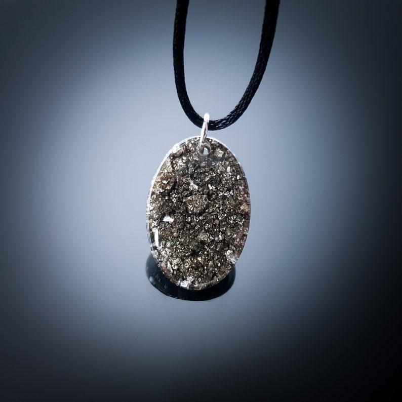May include: A silver oval pendant necklace with a black cord. The pendant is filled with a sparkly, gold-toned material.