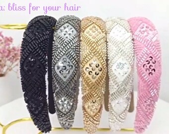 May include: Five embellished headbands in black, silver, gold, white, and pink are displayed on a gold stand. Each headband features a beaded and sequined design. The text "Ananda: bliss for your hair" is visible at the top.
