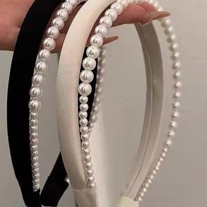 May include: Two hair headbands with pearl embellishments. One headband is black and the other is white.