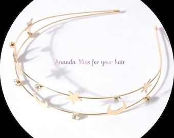 May include: Gold headband with a double row of crescent moons and stars, accented with clear rhinestones. "Ananda bliss for your hair" is written in pink on the headband.