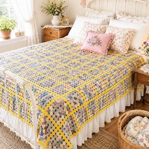 May include: A handmade crochet blanket featuring a repeating pattern of multi-colored floral fabric circles joined together by a bright yellow yarn border. The blanket is draped over a white metal bed frame, covering a white bed skirt and pillows.