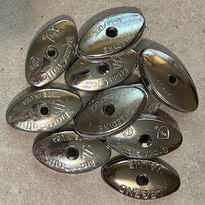 May include: A collection of shiny, silver-colored oval-shaped valve handles. The handles have a central hole and text that reads "Brasscraft", "Teledyne", "Legend Valve", and "Made in USA".
