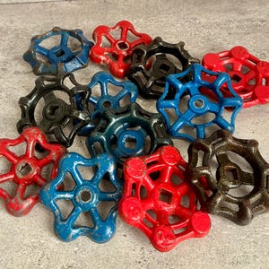 May include: A collection of vintage valve handles in various colors, including red, blue, and black. The handles have a star-shaped design with a central hole. The handles are made of metal and show signs of wear.