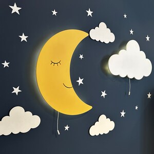 May include: A yellow crescent moon wall light with a smiling face and closed eyes, surrounded by white clouds and stars on a dark blue background.