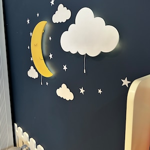 May include: A yellow crescent moon and white cloud wall decor with a string of white stars on a dark blue background. The moon and cloud are 3D and have a light inside.