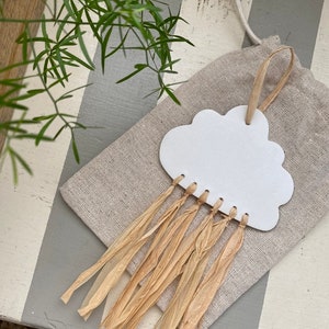 May include: White ceramic cloud with a fringe of natural raffia hanging from a burlap bag. The cloud has a hole at the top for hanging.