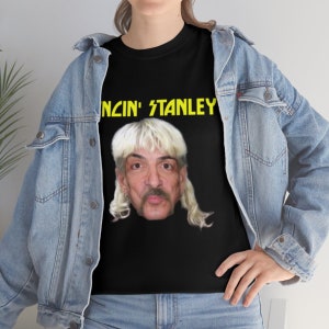 May include: Black t-shirt with a yellow graphic of a man with long blonde hair and a mustache. The text "Dancin' Stanley" is above the image.