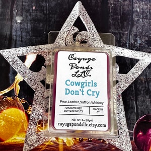May include: A purple soy wax melt in a clear plastic container with the text "Cayuga Ponds LLC. Cowgirls Don't Cry Pear, Leather, Saffron, Whiskey Hand-Poured Soy Wax Melts Made in CT Net Wt. 3oz (85g) cayugapondsllc.etsy.com"
