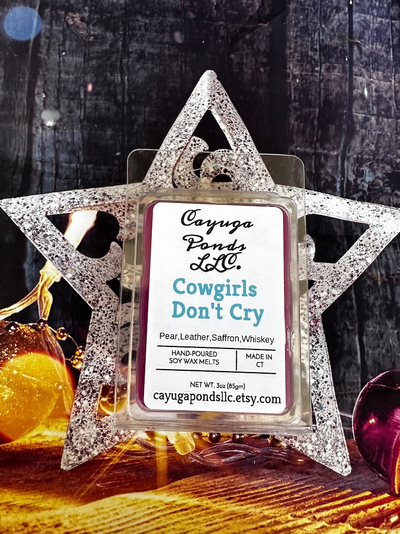 May include: A purple soy wax melt in a clear plastic container with the text "Cayuga Ponds LLC. Cowgirls Don't Cry Pear, Leather, Saffron, Whiskey Hand-Poured Soy Wax Melts Made in CT Net Wt. 3oz (85g) cayugapondsllc.etsy.com"