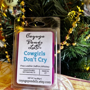 May include: A purple soy wax melt in a clear plastic container. The label reads "Cayuga Ponds LLC. Cowgirls Don't Cry Pear, Leather, Saffron, Whiskey Hand-Poured Soy Wax Melts Made in CT Net Wt. 3oz (85gm) cayugapondsllc.etsy.com"