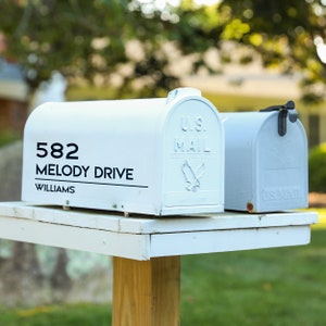 May include: White mailbox with a black address label that reads "582 Melody Drive Williams" and a U.S. Mail logo. The mailbox is mounted on a white wooden post.