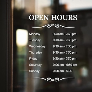 May include: A white sign with black text listing open hours for a business. The sign says "OPEN HOURS" at the top and lists the days of the week with corresponding hours of operation. For example, Monday: 9:30 am - 7:30 pm.
