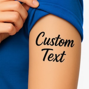 May include: A close-up of an arm with a black tattoo that says "Custom Text". The arm is partially covered by a blue sleeve. A hand is touching the sleeve.