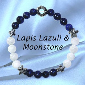 May include: A beaded bracelet featuring alternating sections of dark blue lapis lazuli and white moonstone beads. The design includes silver-toned metal charms shaped like sea turtles and starfish, with a central knot-style silver bead.