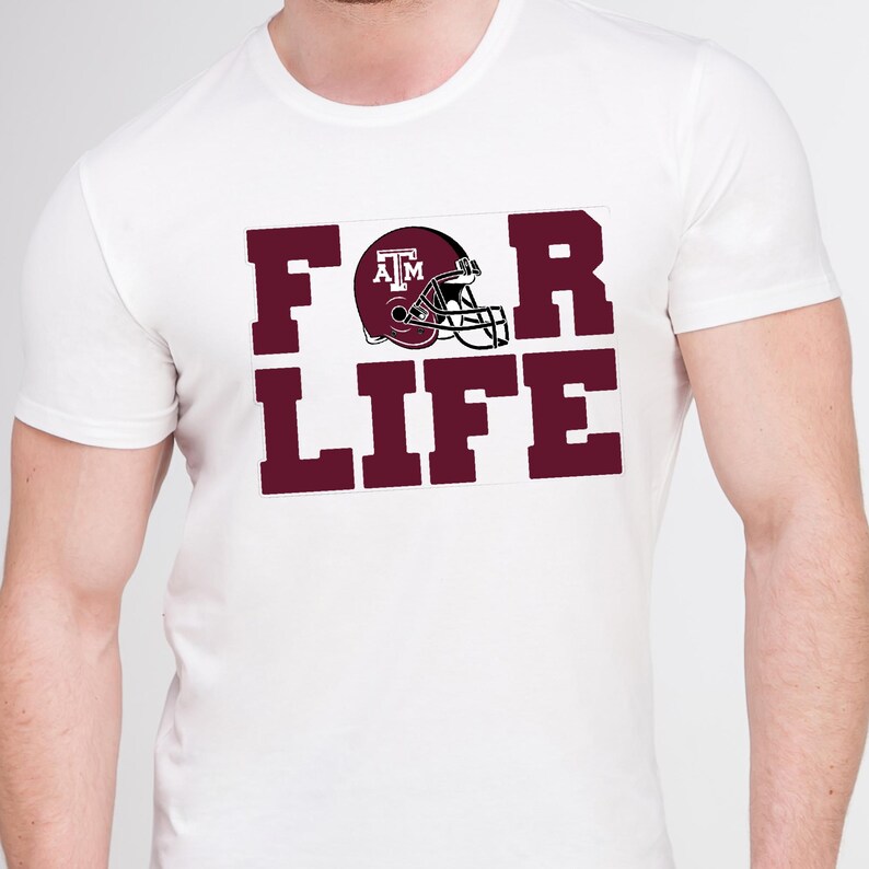 May include: White t-shirt with the maroon text "FOR LIFE" and a maroon football helmet graphic. The helmet has the letters "ATM" on the side. The shirt is a classic crew neck style.