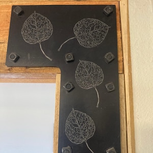 May include: Black metal corner brace with four leaf designs and six black screws. The brace is mounted on a wooden beam.