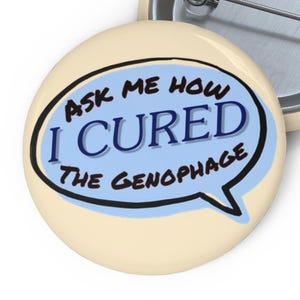 Może przedstawiać: Okrągła przypinka z kremowym tłem i grafiką jasnoniebieskiego dymka. Tekst wewnątrz dymka brzmi "ASK ME HOW I CURED THE GENOPHAGE" i jest napisany ciemnoniebieskimi oraz czarnymi literami. Z tyłu widoczna jest metalowa agrafka.