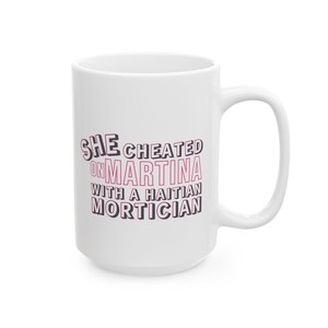 White ceramic mug with bold pink and black text reading “She cheated on Martina with a Haitian mortician,” referencing a Real Housewives of Miami quote.