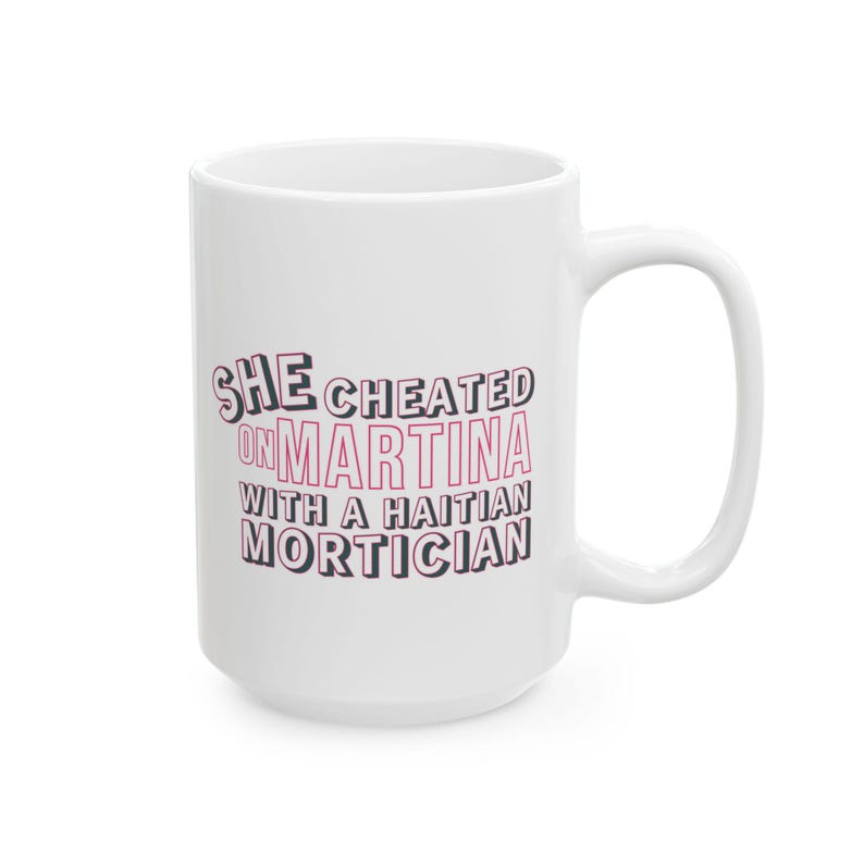 White ceramic mug with bold pink and black text reading “She cheated on Martina with a Haitian mortician,” referencing a Real Housewives of Miami quote.