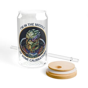 A 16oz clear glass with a stylized image of Garrus from Mass Effect, framed in a circle with the quote “I’m in the middle of some calibrations” in bold, sci-fi inspired font.