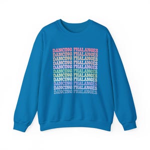 Puede incluir: Una sudadera azul con el texto "DANCING PHALANGES" en un diseño de gradiente arcoíris. El texto se repite varias veces en el centro. La sudadera tiene cuello redondo y mangas largas.