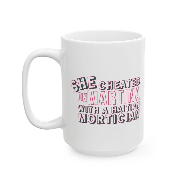 White ceramic mug with bold pink and black text reading “She cheated on Martina with a Haitian mortician,” referencing a Real Housewives of Miami quote.