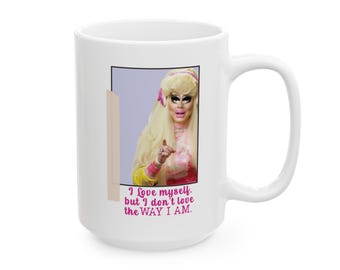 May include: White ceramic mug with a pink and white image of a woman with blonde hair and a pink and white outfit. The text on the mug reads "I love myself, but I don't love the way I am."