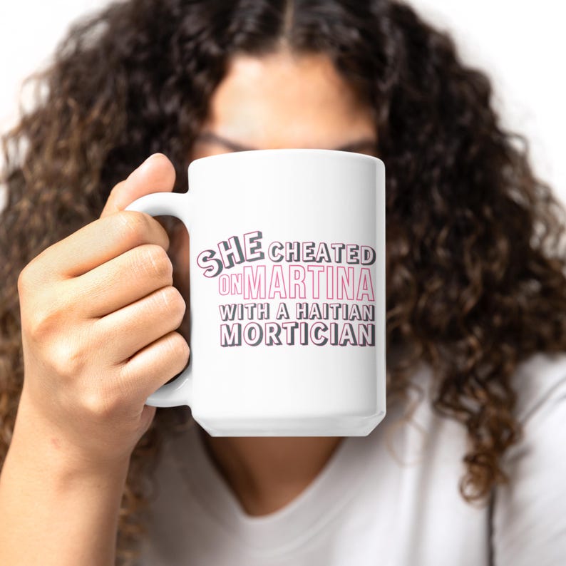 White ceramic mug with bold pink and black text reading “She cheated on Martina with a Haitian mortician,” referencing a Real Housewives of Miami quote.
