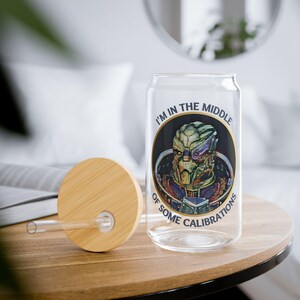 A 16oz clear glass with a stylized image of Garrus from Mass Effect, framed in a circle with the quote “I’m in the middle of some calibrations” in bold, sci-fi inspired font.