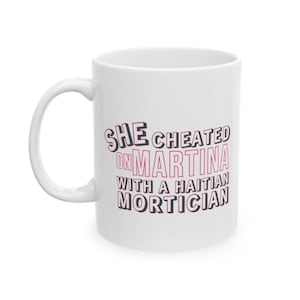 White ceramic mug with bold pink and black text reading “She cheated on Martina with a Haitian mortician,” referencing a Real Housewives of Miami quote.