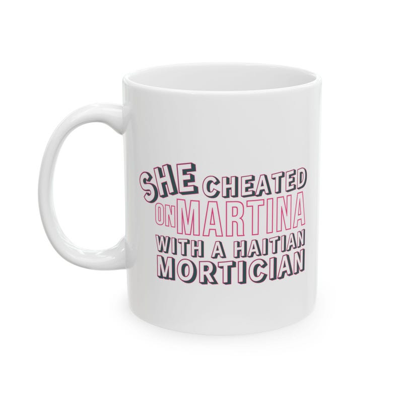 White ceramic mug with bold pink and black text reading “She cheated on Martina with a Haitian mortician,” referencing a Real Housewives of Miami quote.