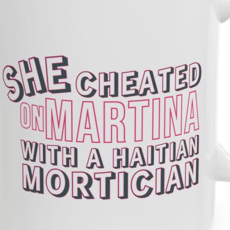 White ceramic mug with bold pink and black text reading “She cheated on Martina with a Haitian mortician,” referencing a Real Housewives of Miami quote.