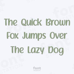 May include: Text-based graphic with the phrase "The Quick Brown Fox Jumps Over The Lazy Dog" in a green, handwritten-style font. The words are centered on a white background. The "font station" logo is at the bottom.