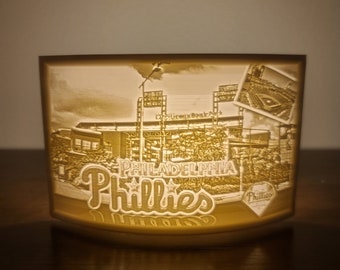 May include: A white ceramic night light with a 3D image of Citizens Bank Park, home of the Philadelphia Phillies. The image includes the words "Philadelphia Phillies" and a diamond-shaped logo with the word "Phillies" inside.