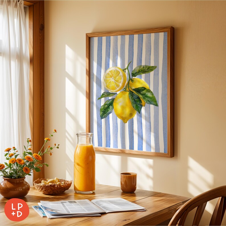 May include: A framed watercolor print of lemons with green leaves against a blue and white striped background. The print is in a wooden frame. A glass bottle of orange juice, a small brown cup, and a flower arrangement are on a wooden table.