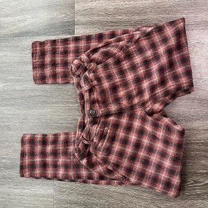May include: Red and black checked trousers with a button fastening. The trousers are made from a soft, comfortable fabric.