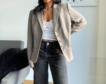 May include: A woman wearing a light brown blazer over a white lace cami top and black jeans with distressed knees.