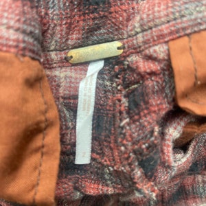 May include: Red and black plaid flannel shirt with a Free People tag. The shirt has a brown fabric trim on the left side.