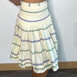 May include: A white skirt with green and purple stripes. The skirt is pleated and has a fitted waistband.