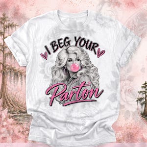 Könnte beinhalten: Ein weißes T-Shirt mit einer schwarz-weißen Grafik einer Frau mit voluminösem Haar, die eine rosa Kaugummiblase bläst. Der Text lautet I BEG YOUR Parton in schwarzer und rosa Schrift, akzentuiert durch zwei kleine rosa Herzen an den Seiten.