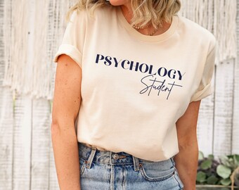 May include: A cream colored t-shirt with the text "Psychology Student" in navy blue lettering. The text "Student" is in a handwritten font.