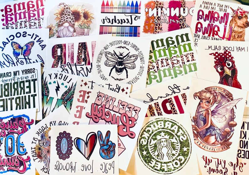 May include: A collection of various printed designs on white paper. The designs include text, illustrations, and logos. Some feature phrases like "Anti-Social" and "Feeling Lucky." Others showcase a bee, a fairy, and a Starbucks logo.