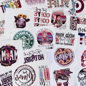 May include: A collection of various printed designs on white paper. The designs include a cow with a sunflower crown, coffee-themed text, a Starbucks logo, and a woman meditating. Other designs feature text like "MAMA" and "HOT GIRL".