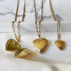 May include: Three gold heart-shaped locket necklaces with delicate chains. The lockets have intricate designs and are open to reveal a space for a photo or small memento.