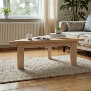 May include: A light oak triangular coffee table with four legs. A white mug and an open book are on the table, along with a stack of books and a small potted plant. The table is placed on a beige rug. The table is approximately 100 cm long.