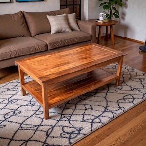 Peut inclure: Une table basse rectangulaire en bois avec une étagère inférieure. La table est en bois brun clair avec une finition brillante. Elle repose sur un tapis à motifs. Un canapé marron et une table d'appoint sont en arrière-plan.