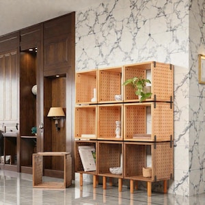 Puede incluir: Una estantería cúbica de madera con nueve compartimentos abiertos. La unidad está hecha de madera de color claro con un diseño perforado. Los estantes están dispuestos en una cuadrícula de tres por tres y están soportados por patas cortas y redondeadas. Se colocan objetos decorativos en los estantes.