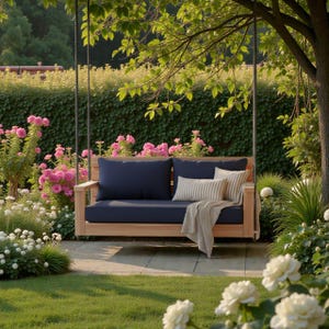 May include: A wooden garden swing with navy blue cushions and a striped cushion suspended from a tree. The swing is set in a garden with pink and white flowers, green grass, and a hedge in the background.