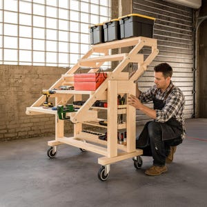 May include: A wooden rolling workbench with multiple shelves, drawers, and a top platform. It features a variety of tools, including a drill, clamps, and a toolbox. Three black storage bins sit on top. The workbench is on wheels.